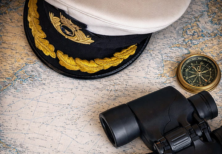 A Captain's hat, binocular and compass sitting on top of a map